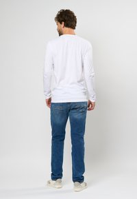 Camicia bianca a maniche lunghe abbinata a jeans blu, con vestibilità standard e design casual, mostrata da dietro. Sneakers casual incluse.