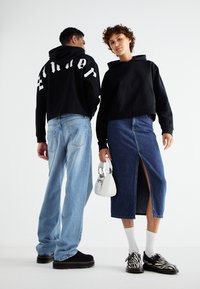 Svart cropped hettegenser med hvit tekst, lyseblå vide jeans, denimskjørt med frontslitt, hvit håndveske og zebra-mønstrede sko.