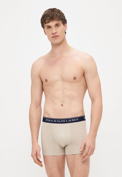 Smėlio spalvos bokseriai su tamsiai mėlynu liemeniu, ant kurio yra „POLO RALPH LAUREN“ logotipas. Minkšta, tampri medžiaga ir aptakus dizainas, ilgio iki vidurio šlaunies.