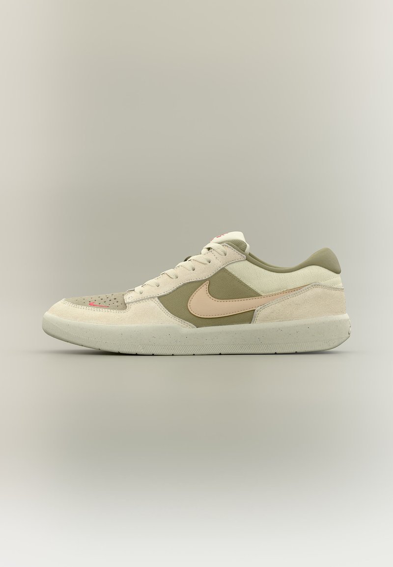 Beiger und olivfarbener Nike-Sneaker mit niedrigem Schaft aus Wildleder- und Stoffpaneelen, hellrosa Swoosh und gesprenkelter Gummisohle auf neutralem Hintergrund.