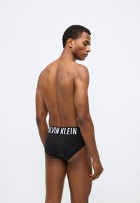 Μαύρα εσώρουχα Calvin Klein με φαρδύ ελαστικό ζωνάκι που εμφανίζει το όνομα της μάρκας σε λευκό χρώμα. Λείος ύφασμα με σφιχτή εφαρμογή.