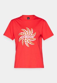 Röd bomullströja med en vit spiralgrafik som har flerfärgade triangulära mönster och "adidas"-logotypen i centrum.