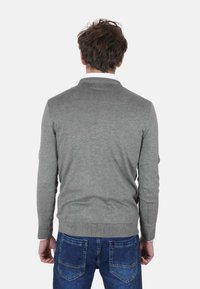 Maglione grigio visto da dietro, con scollo rotondo e orlo a coste, abbinato a jeans di denim blu. Design semplice e casual.