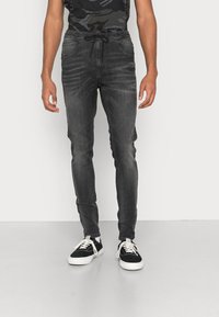 Tmavě šedé joggingové kalhoty vyrobené z denimu, s elastickým pasem a tkaničkou, a bočními kapsami. V kombinaci s černými teniskami.