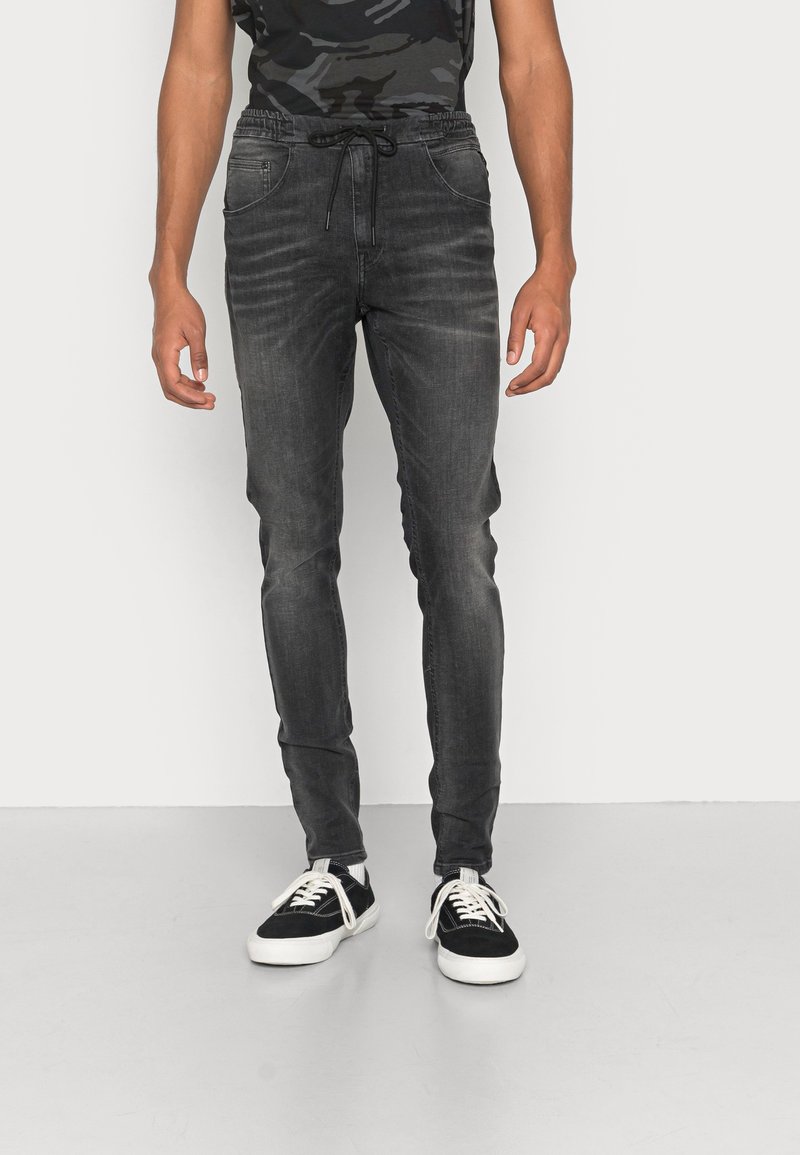 Tmavě šedé joggingové kalhoty vyrobené z denimu, s elastickým pasem a tkaničkou, a bočními kapsami. V kombinaci s černými teniskami.