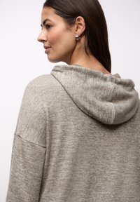 Jasnoszara bluza z kapturem o luźnym kroju, miękkiej fakturze i lekko melanżowym wyglądzie, z szerokimi rękawami i zaokrąglonym kapturem.