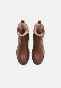 Bottines marron à semelles noires, avec des fermetures éclair latérales et une doublure en fausse fourrure beige, vues de dessus sur un fond blanc.