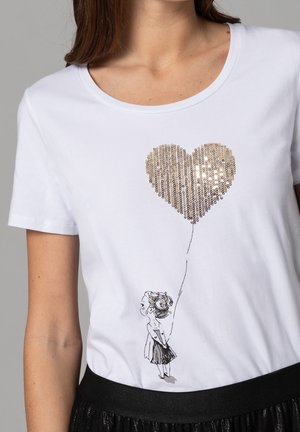 Camiseta blanca de algodón con diseño de corazón dorado de lentejuelas y dibujo lineal negro de una niña sosteniendo un globo, con cuello redondo.
