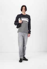 Gray and white striped knit sweater with ribbed texture, light gray jeans, and black sneakers. Model carries a small black shoulder bag.