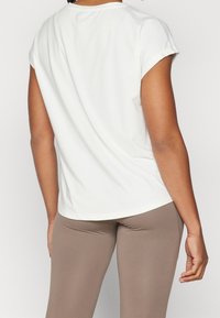 Top blanco de manga corta con escote redondo, textura suave y corte relajado, combinado con leggings beige.