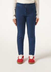 Leggings de mezclilla azul con una cinturilla elástica, que cuentan con dos bolsillos frontales, combinados con zapatillas rojas con cordones blancos y una suela marrón.