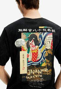 Juodas medvilninis marškinėliai su spalvingu japonišku grafikų dizainu ant nugaros, su teksto elementais ir išsikišusiu kabuki personažo iliustracija.