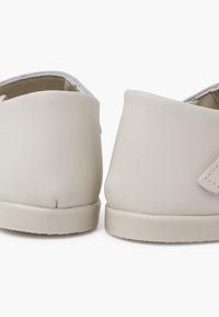 Zapatos de cuero blancos con una textura suave, forma redondeada y diseño minimalista. Presentan un pequeño detalle cosido en el costado.