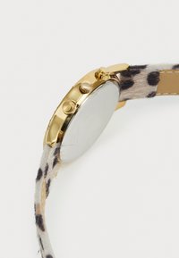 Goldfarbene Uhrengehäuse mit drei seitlichen Knöpfen und einem strapazierfähigen Tierfell-Print-Armband, seitlich auf einem weißen Hintergrund gezeigt.