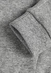 Gefalteter grauer Strickstoff, der die Manschette und die Ärmeldetails eines gemütlichen Pullovers oder Sweatshirts zeigt.
