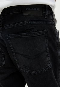 Czarne dżinsy z przetarciami i dwiema tylnymi kieszeniami. Mają textured metkę w pasie z napisem "PULL&BEAR."