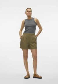 Grijze geribbelde mouwloze top gecombineerd met olijfgroene geplooide shorts, met zijzakken en bruine sandalen met een dikke zwarte zool.