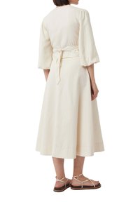 Cremfarbendes, knielanges Kleid mit puffärmeligen Ärmeln und einem gebundenen Gürtel in der Taille. kombiniert mit hellbraunen Riemchensandalen. Schlichtes Design, weicher Stoff.