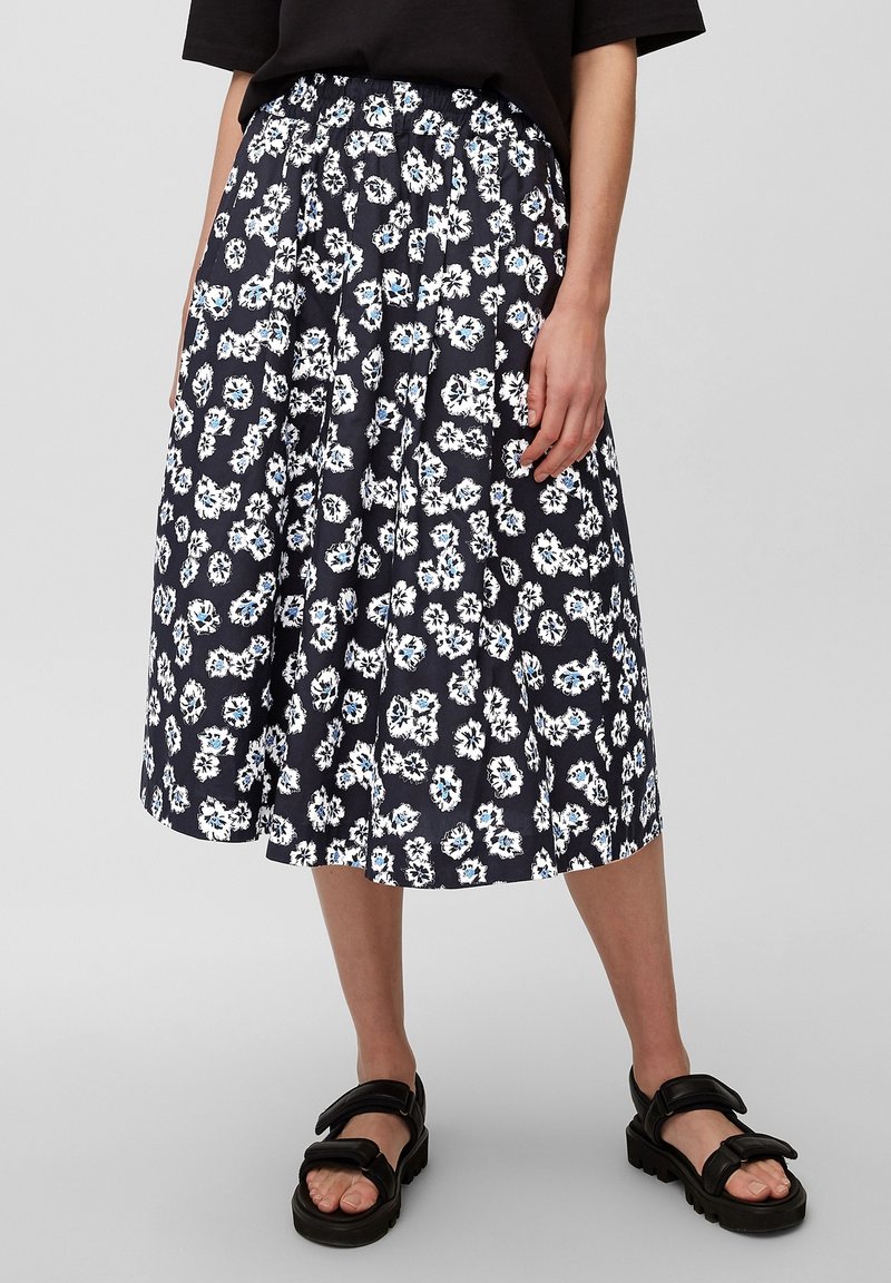 Falda midi floral en azul marino con patrón floral en blanco y azul, diseño plisé, cinturilla elástica, combinada con sandalias negras de suela gruesa.