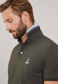 Ciemnozielona koszulka polo z zapięciem na trzy guziki, haftowanym logo oraz kołnierzykiem w niebiesko-białe paski.