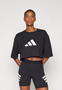 Fekete cropped póló nagy fehér adidas logóval. Fekete sorttal párosítva, amelynek oldalán három fehér csík található. Sima textúra.