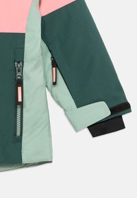 Manga de chaqueta verde y rosa con forro interior verde claro, puño elástico negro, bolsillo con cremallera y cierre de tira de Velcro en la muñeca.