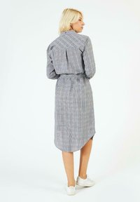 Robe chemise à carreaux gris avec un col, des manches longues, une taille ceinturée et un ourlet incurvé. Plis à l'arrière et détails de boutons remarquables.