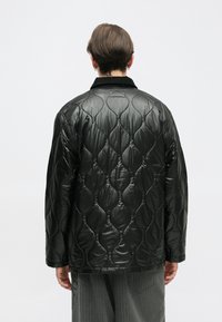Czarna pikowana kurtka z błyszczącym, teksturowanym wykończeniem i wzorem fal. Długie rękawy i klasyczny kołnierz dopełniają całość.