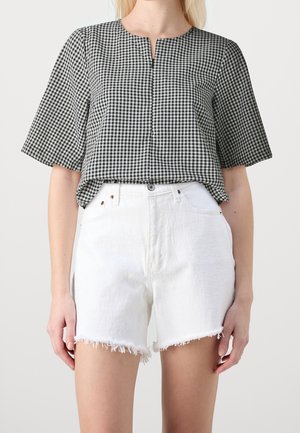 Zwart-wit gingham top met korte mouwen en een ronde halslijn, gecombineerd met witte denim shorts met een rafelrand.