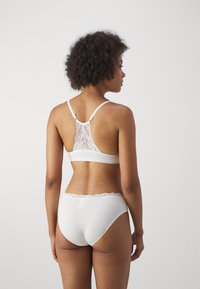 White lingerie set featuring a bralette with lace back detail and adjustable straps, paired with matching brief with lace trim.