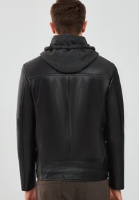 Veste en cuir noir avec une capuche grise. Le design présente une texture lisse, une silhouette ajustée et des détails de couture subtils au dos.