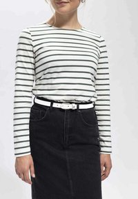 Gestreiftes Langarmhemd in Weiß und Grün, kombiniert mit einem schwarzen Denimrock und einem weißen Gürtel. Das Outfit zeichnet sich durch klare Linien und ein einfaches Design aus.