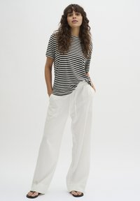 Black and white striped t-shirt paired with loose white pants. The outfit features a relaxed fit and lightweight fabric, detailed with a drawstring.