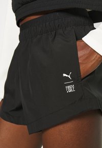 Pantalones cortos deportivos negros hechos de un material ligero y elástico. Las características incluyen una cintura elástica y acentos de logo en blanco.