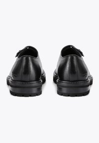 Scarpe in pelle nera con una finitura liscia, punta rotonda, design minimale, caratterizzate da una spessa suola in gomma nera e dettagli di cucitura discreti.