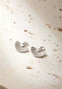 Boucles d'oreilles en argent en forme de éventail avec des détails rainurés et un accent circulaire au centre. Présentées sur une surface texturée claire.