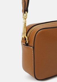 Ruskea nahkalaukku, jossa on teksturoitu pinta, kultainen vetoketju ja musta kontrastireunus. Varustettu metallikiinnikkeellä ja ompeleilla.