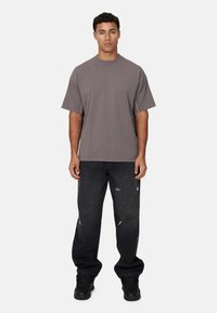 Grijze oversized t-shirt met een ronde hals, korte mouwen en contrasterende stiksels, gecombineerd met zwarte distressed jeans en zwarte sneakers.