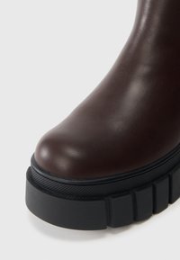 Brune lær ankelsko med en rund tå, med en tykk svart gummi såle og teksturerte detaljer på kanten av sålen.