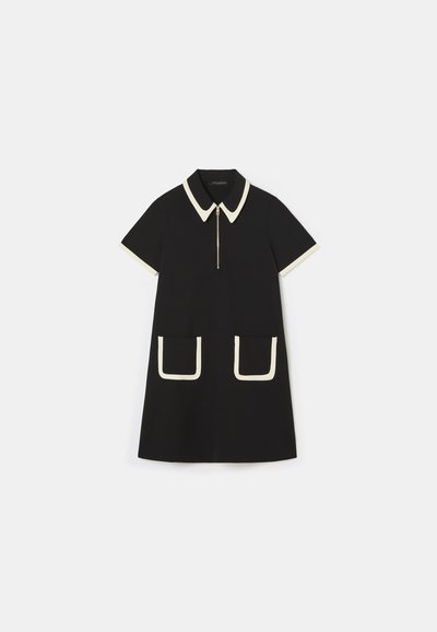 Vestido negro con mangas cortas, cuello y ribete blanco en contraste, cierre de cremallera y dos grandes bolsillos frontales contorneados en blanco.