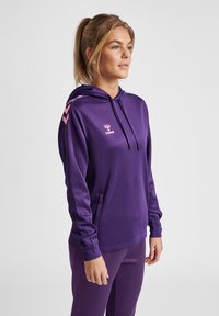 Paarse hoodie van een gladde stof met een trekkoordkap. Voorzien van roze chevron accenten op de schouders en een voorkant zak. Logo op de borst.