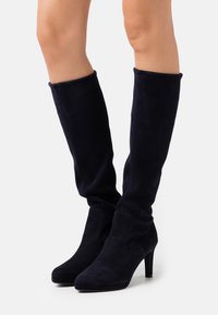 Bottes montantes en daim bleu marine à texture lisse, avec un bout pointu et un talon haut et fin. Design minimaliste, sans ornements visibles.