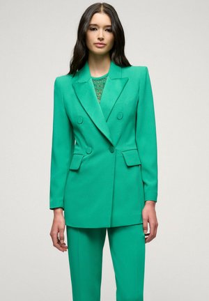 Green tailored blazer with double-breasted button closure, notched lapels, and matching trousers. Smooth, textured fabric with sleek fit.