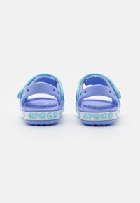 Purple open-back sandals made of rubber with adjustable straps and a textured footbed, featuring "crocs" logo in light blue on the sole.