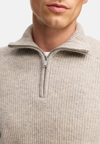 Helle beigen Zip-Up-Pullover mit Rippstruktur und hohem Kragen. Silberner Metallreißverschluss am Hals, mit einem schlichten, unauffälligen Design.