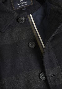 Abrigo de lana a cuadros en negro y gris con cuello alto, con botones negros y un forro acolchado azul marino con acentos de rayas.