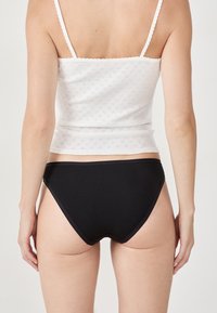 Culottes en coton noir avec une texture lisse, présentant un design taille basse et des détails de surpiqûre contrastants. Débardeur blanc avec un motif texturé.