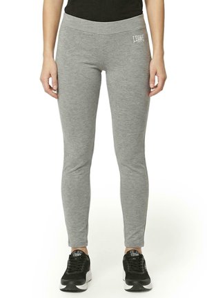 Un mannequin porte un legging Leone gris ajusté, orné d’un petit logo blanc, et des baskets noires sur un fond blanc.
