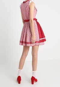 Robe rouge et rose avec un corsage ajusté, jupe évasée, motif étoile, bordure en dentelle blanche et ceinture rouge. Associée à des talons rouges et des chaussettes blanches.