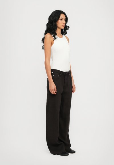 Top sin mangas ajustado blanco combinado con pantalones anchos negros que tienen una cintura con cordón y bolsillos frontales. Calzado negro complementa el conjunto.